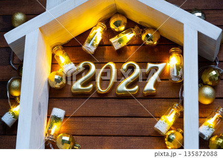 Golden figures number 2027 and tiny home on background of cozy windows of a house with warm light with festive decor of stars,snow and garlands. Greeting card, Happy New Year, cozy home Golden figures number 2027 and tiny home on background of cozy windows of a house with warm light with festive decor of stars,snow and garlands. Greeting card, Happy New Year, cozy home 135872088