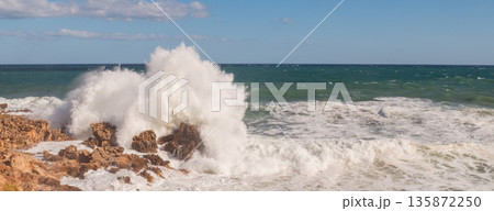 Stormy seascape with waves crashing against rocky shore and high white foam splashes. 135872250