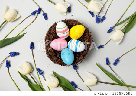 Easter colored painted eggs in bird nest with white tulips, and blue muscari on gray background. Easter and spring concept. Spring background Easter colored painted eggs in bird nest with white tulips, and blue muscari on gray background. Easter and spring concept. Spring background 135872590