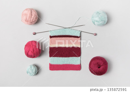 Brown beige vinous and turquoise piece of striped knitting with knitting needles and balls of thread on gray background. Homemade needlework and knitting of warm, clothes and toys. Concept creativity Brown beige vinous and turquoise piece of striped knitting with knitting needles and balls of thread on gray background. Homemade needlework and knitting of warm, clothes and toys. Concept creativity 135872591