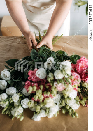 Person gathers bundles of pink and white lisianthus flowers on craft paper. Support local florists, flower farm-to-shop, urban florist. 135873653