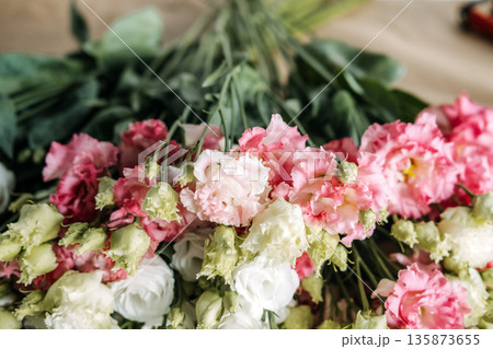 Bunches of pink and white lisianthus flowers lie flat on brown paper. Eryngium alpium, goldenrod, floristry workshop, slow living, hand-gathered bouquets. 135873655