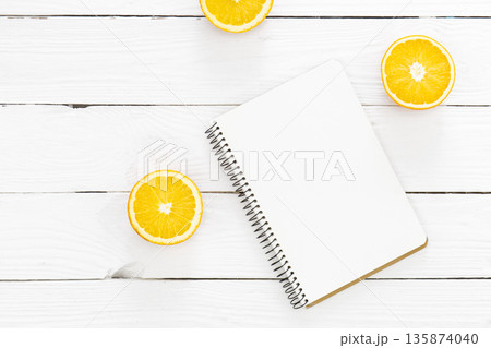 Blank notebook and halves of oranges on a white wooden background, flat lay. Blank notebook and halves of oranges on a white wooden background, flat lay. 135874040