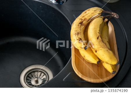 A bunch of ripe yellow bananas in the kitchen near the sink. A bunch of ripe yellow bananas in the kitchen near the sink. 135874190