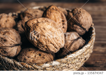 Close-up, whole walnuts in a wicker bowl on a wooden background. 135874347