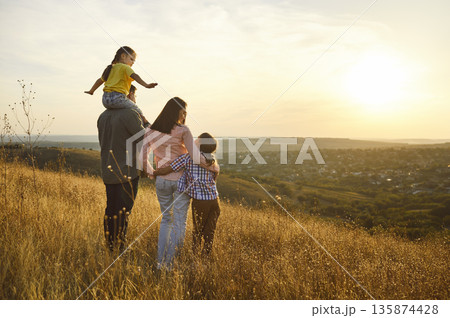 Happy family embracing at sunset in a golden meadow, enjoying nature together 135874428