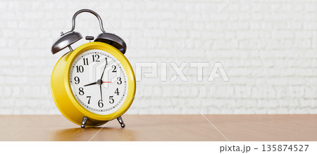 Yellow Alarm Clock on Wooden Table Against White Brick Wall Background, Bright Morning Time Concept Yellow Alarm Clock on Wooden Table Against White Brick Wall Background, Bright Morning Time Concept 135874527