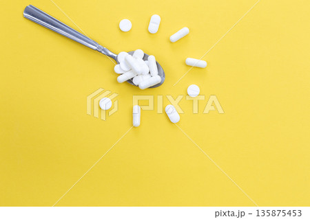 White pills in spoon in the shape of a flower on a yellow background, flat lay. White pills in spoon in the shape of a flower on a yellow background, flat lay. 135875453