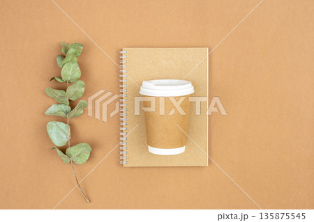 Craft paper coffee cup, notebook and eucalyptus sprig on eco background, flat lay. 135875545