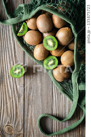 Fruits of kiwi in a mesh bag on a wooden background, top view, rustic style, 135875723