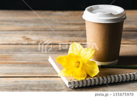 Paper disposable cup, notebook and yellow flower on a wooden blurred background. Paper disposable cup, notebook and yellow flower on a wooden blurred background. 135875970
