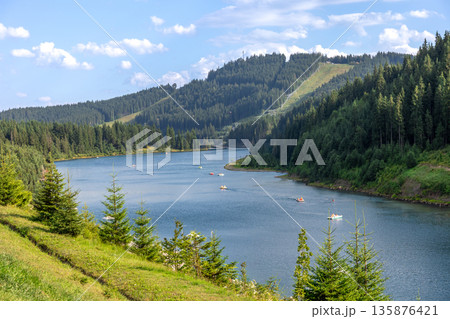 Mountain lake with paddle boats and pine slopes. Summer leisure on water. 135876421