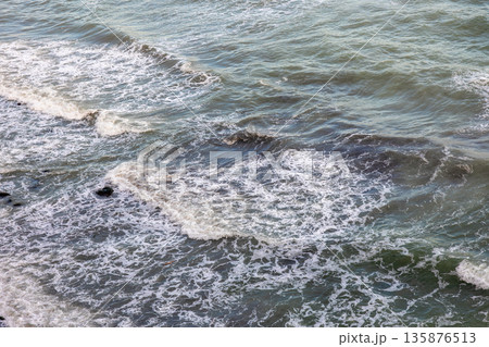 Foamy sea waves on a rocky shore. Motion and texture of water. 135876513