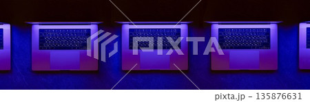 Row of laptops in blue neon for IT teams. Cyber tech scene. 135876631