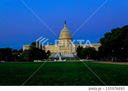People stroll on grass near US Capitol building as lights shine in early evening sky in Washington DC 135876893