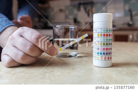 A man in the kitchen tests tap water quality with a test strip. Home testing for drinking water safety, pH, chlorine, and chemical contaminants. 135877160