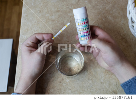 A man in the kitchen tests tap water quality with a test strip. Home testing for drinking water safety, pH, chlorine, and chemical contaminants. A man in the kitchen tests tap water quality with a test strip. Home testing for drinking water safety, pH, chlorine, and chemical contaminants. 135877161