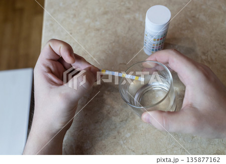 A man in the kitchen tests tap water quality with a test strip. Home testing for drinking water safety, pH, chlorine, and chemical contaminants. A man in the kitchen tests tap water quality with a test strip. Home testing for drinking water safety, pH, chlorine, and chemical contaminants. 135877162