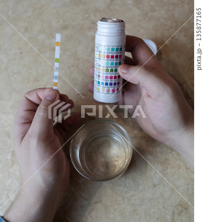 A man in the kitchen tests tap water quality with a test strip. Home testing for drinking water safety, pH, chlorine, and chemical contaminants. A man in the kitchen tests tap water quality with a test strip. Home testing for drinking water safety, pH, chlorine, and chemical contaminants. 135877165