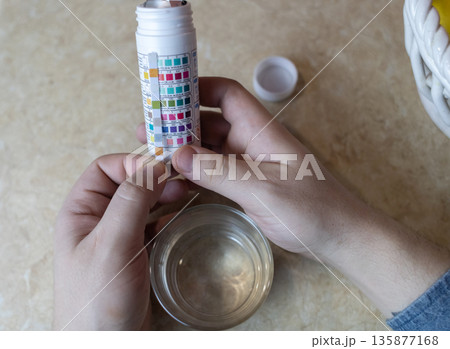A man in the kitchen tests tap water quality with a test strip. Home testing for drinking water safety, pH, chlorine, and chemical contaminants. 135877168