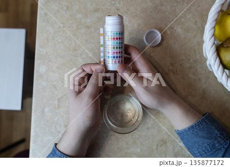 A man in the kitchen tests tap water quality with a test strip. Home testing for drinking water safety, pH, chlorine, and chemical contaminants. 135877172