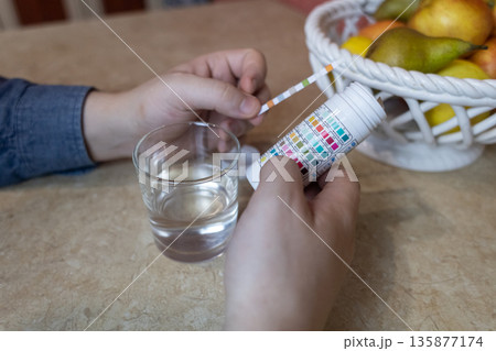 A man in the kitchen tests tap water quality with a test strip. Home testing for drinking water safety, pH, chlorine, and chemical contaminants. A man in the kitchen tests tap water quality with a test strip. Home testing for drinking water safety, pH, chlorine, and chemical contaminants. 135877174