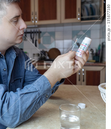 A man in the kitchen tests tap water quality with a test strip. Home testing for drinking water safety, pH, chlorine, and chemical contaminants. A man in the kitchen tests tap water quality with a test strip. Home testing for drinking water safety, pH, chlorine, and chemical contaminants. 135877180