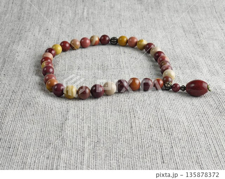 Prayer beads made of mukaite jasper on a burlap background. These 33-bead prayer beads are traditionally used in Christian and Islamic prayer practices 135878372