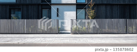 A modular grey wooden and steel fence stands prominently in front of a modern townhouse, showcasing simple lines and a clean design that complements the suburban setting, banner 135878602