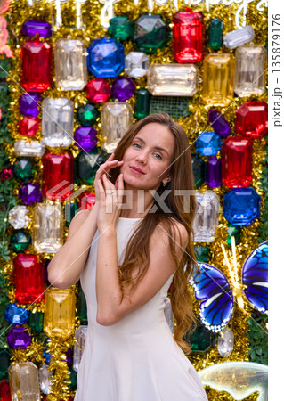 Young woman smiling and posing in front of colorful Christmas gem wall backdrop Young woman smiling and posing in front of colorful Christmas gem wall backdrop 135879176