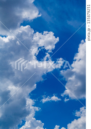 Vertical photo of white clouds against a blue sky, the edges of which are illuminated by lateral sunlight. Weather phenomena, synoptic forecasts. Natural environment theme Vertical photo of white clouds against a blue sky, the edges of which are illuminated by lateral sunlight. Weather phenomena, synoptic forecasts. Natural environment theme 135879251