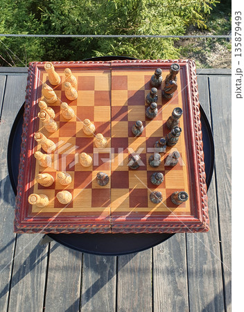 Wooden carved chessboard with pieces, on a black table in the open air with a panoramic view of the Carpathians. Light and dark wooden chess pieces. Mountain landscape. theme of intellectual games 135879493