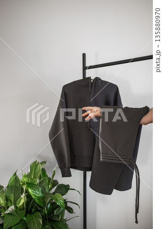 Hoodie and sweatpants displayed on rack with plant in a modern room 135880970