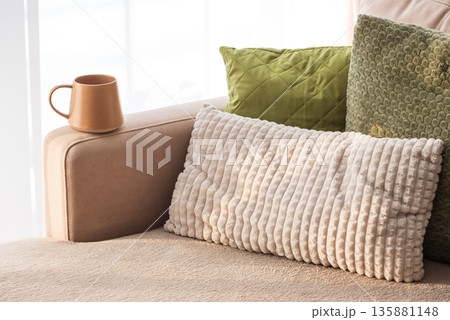Ceramic Coffee Mug on Sofa Armrest with Textured Pillows. Cozy Home Interior 135881148