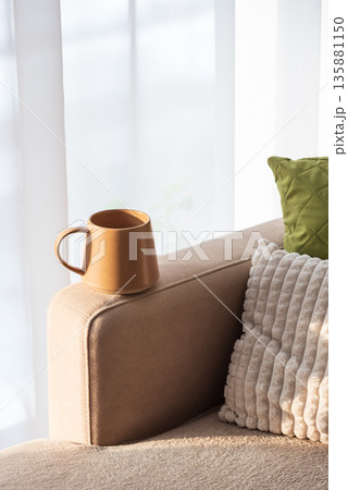 Ceramic Coffee Mug on Sofa Armrest with Textured Pillows. Cozy Home Interior Ceramic Coffee Mug on Sofa Armrest with Textured Pillows. Cozy Home Interior 135881150