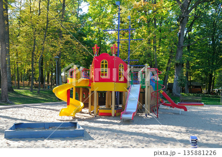Children's outdoor play complex with slides and sandbox in a forest setting. Children's outdoor play complex with slides and sandbox in a forest setting. 135881226