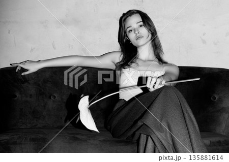 Elegant young woman holding flower on sofa Elegant young woman holding flower on sofa 135881614