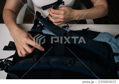 Young woman adjusting strap on modern stylish urban backpack, getting ready for commute or travel adventure, embodying convenience and functionality for active lifestyle, close-up. 135881615
