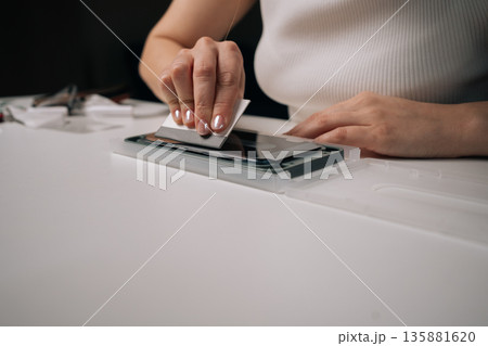 Skilled technician carefully applying smartphone screen protector with specialized machine, using squeegee for precise, bubble-free installation. Concept of mobile phone maintenance and service. 135881620