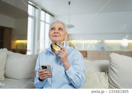 Senior woman shopping online with smartphone paying with credit card at home Old lady buying on Internet enter credit card details Online shopping delivery service. Older generation modern tech usage 135881805