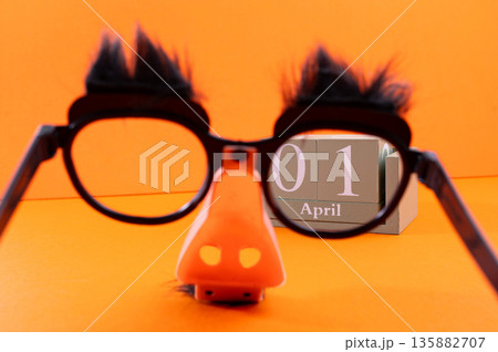Calendar with clown wig, funny glasses and sequins on brown background. April Fools Day 135882707