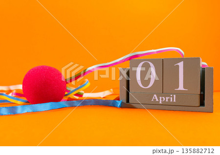 Calendar with clown wig, funny glasses and sequins on brown background. April Fools Day Calendar with clown wig, funny glasses and sequins on brown background. April Fools Day 135882712