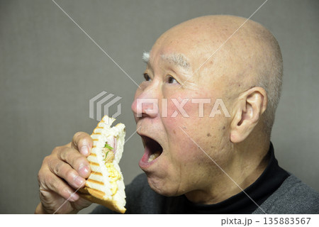 ホットサンドを笑顔で食べる老人 135883567