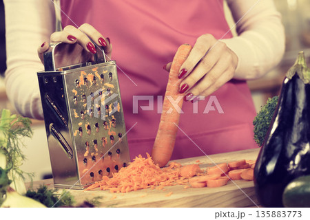 Woman grating carrot on metal grater 135883773