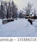 Snow-covered park scene featuring a wooden bridge leading to a charming rustic cabin 135884218