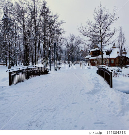 Snow-covered park scene featuring a wooden bridge leading to a charming rustic cabin 135884218