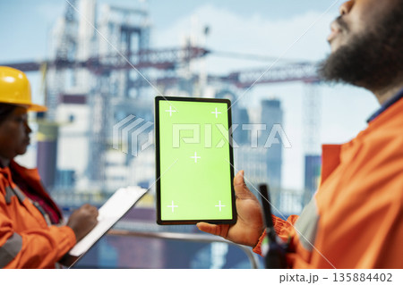Green screen tablet used by offshore platform workers to monitor equipment performance in real time. Drilling rig specialists calibrate gear with asset management system on mockup device, closeup 135884402