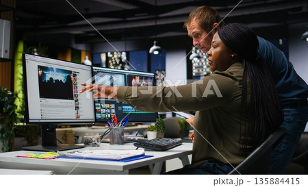 Team of multiethnic videographers editing video shoot in post production, using modern tech and editing software for a creative video project. Modern workspace with dual monitors. Camera A. 135884415