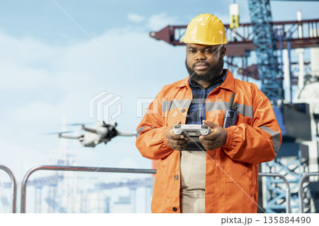 Drilling rig technician using drone to access areas that pose environmental risks to humans from safe distance. Man on offshore platform deck uses remote control UAV to conduct aerial surveys 135884490