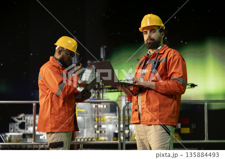 Offshore platform worker uses laptop software during aurora borealis night to forecast gear maintenance needs. Expert analyzes data on notebook dashboard under northern lights to prevent errors 135884493